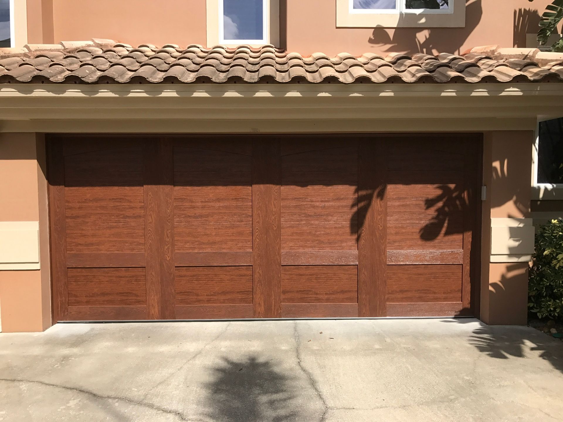 Brown wooden garage door on a tan house with a tile roof.
