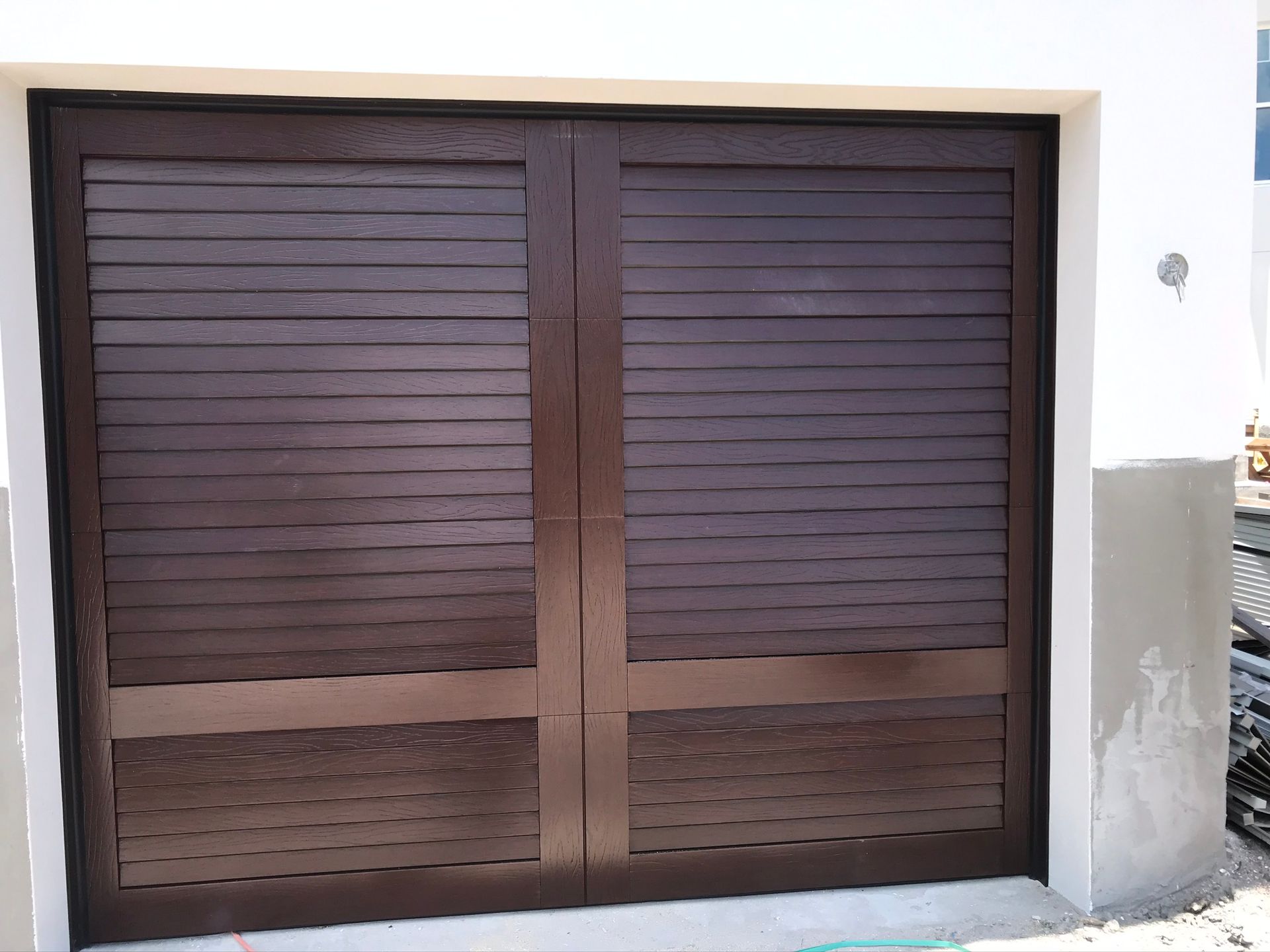 Brown wooden garage doors with horizontal slats, set in a white building.