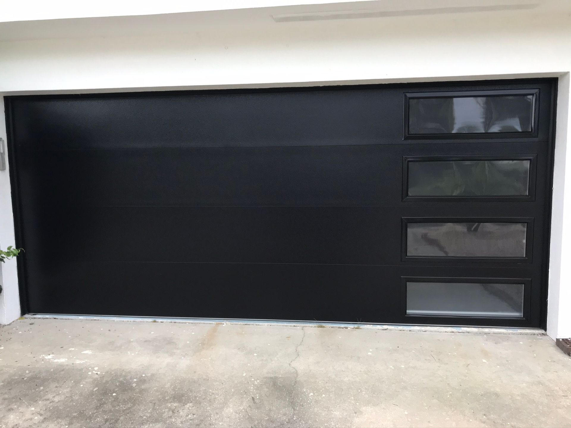 Black garage door with three rectangular glass windows, in a white-walled setting.