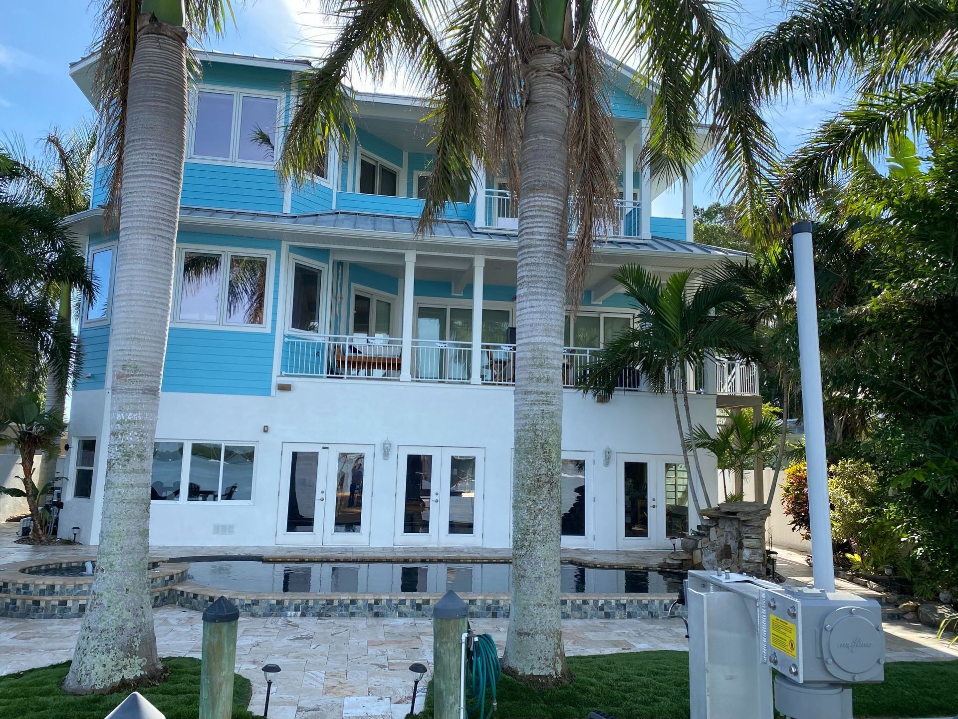 Two-story, blue and white house with palm trees, next to water.