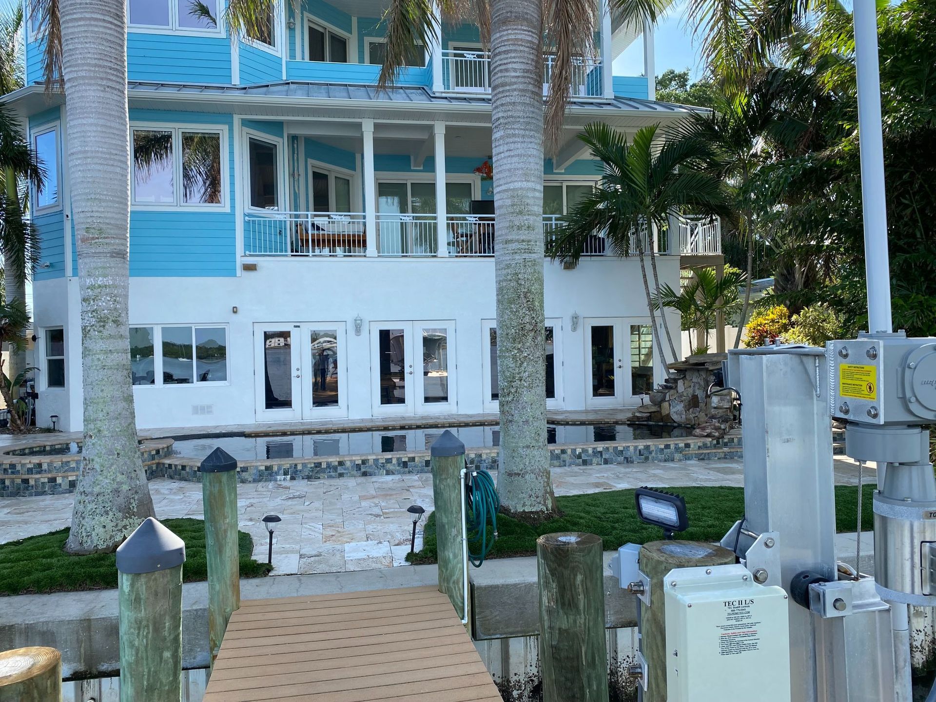 Coastal house with blue and white exterior, palm trees, and dock.