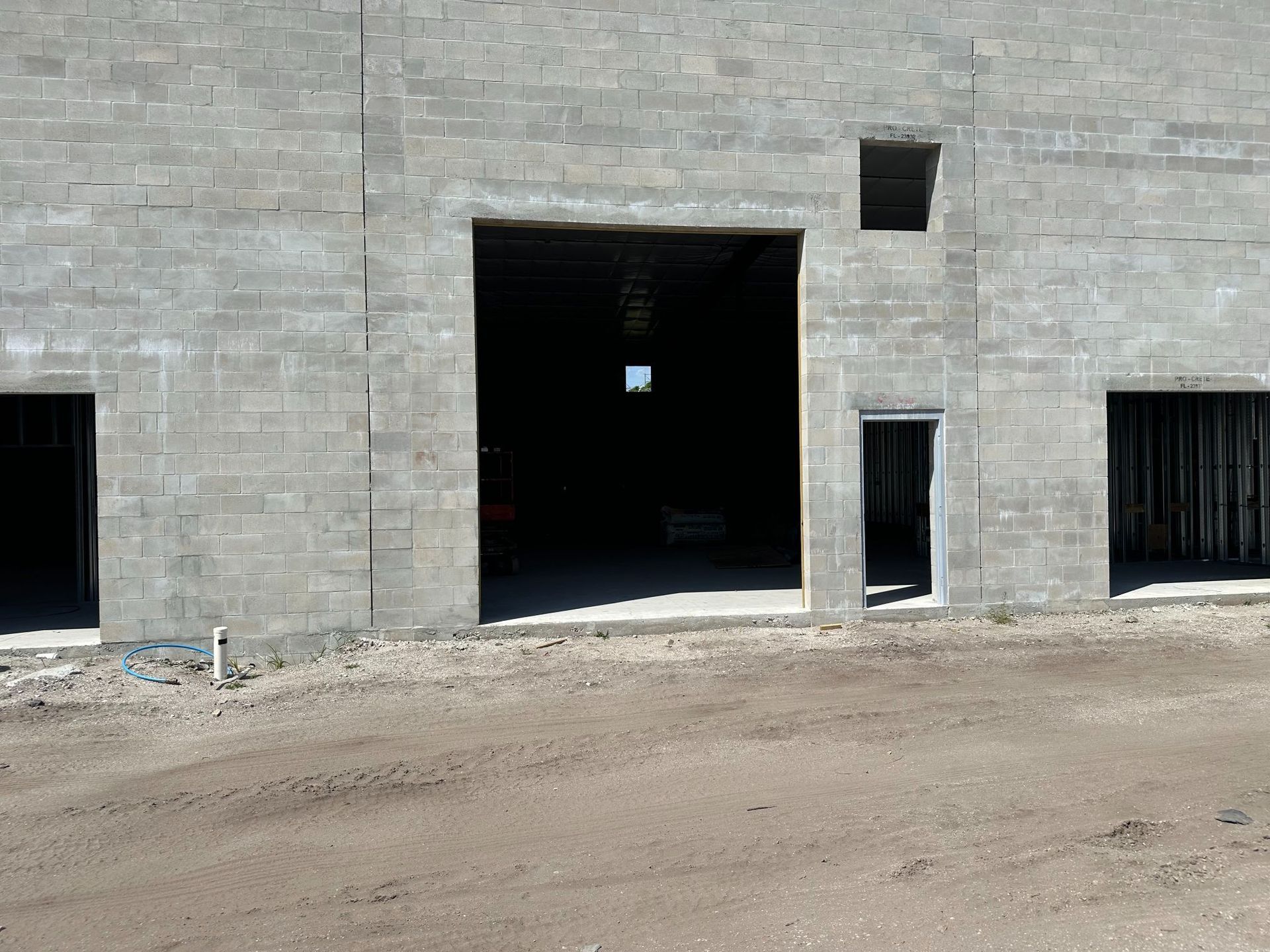 Gray cinder block building with large central doorway and smaller openings, in a dirt lot.