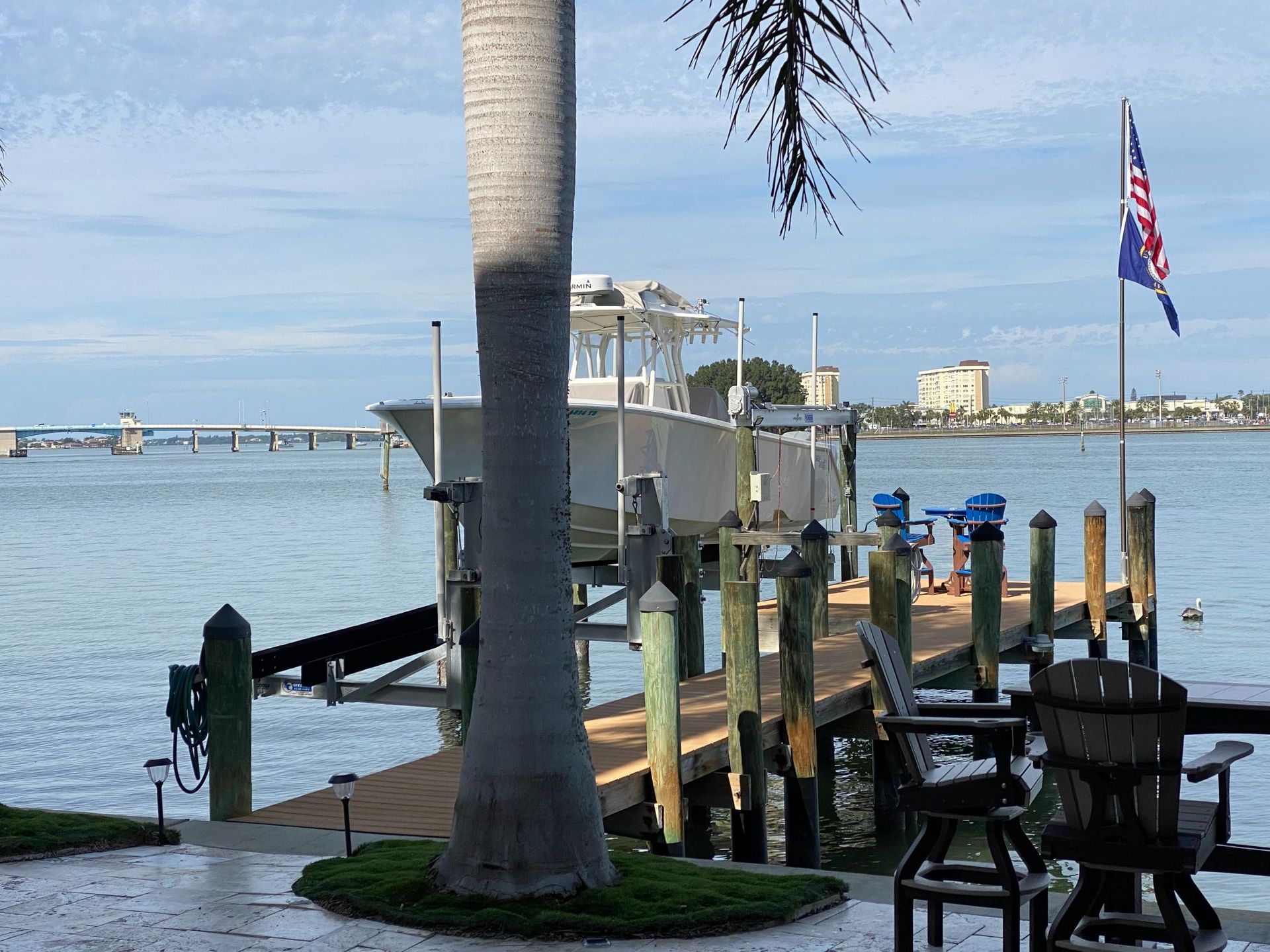 Boat on a lift at a dock, with a bridge and buildings in the background; sunny day.