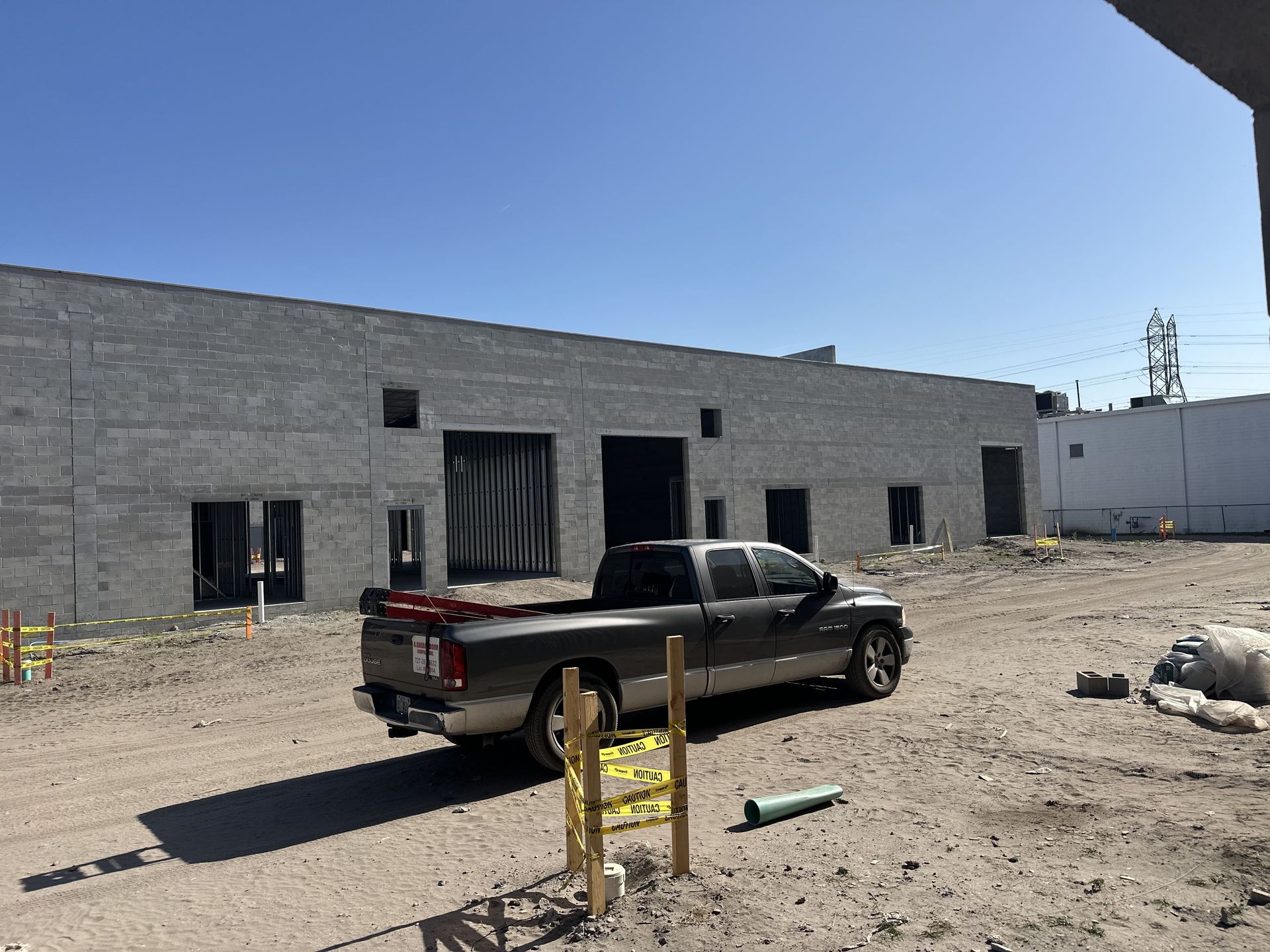 Truck parked in front of a gray brick warehouse under construction on a sunny day.