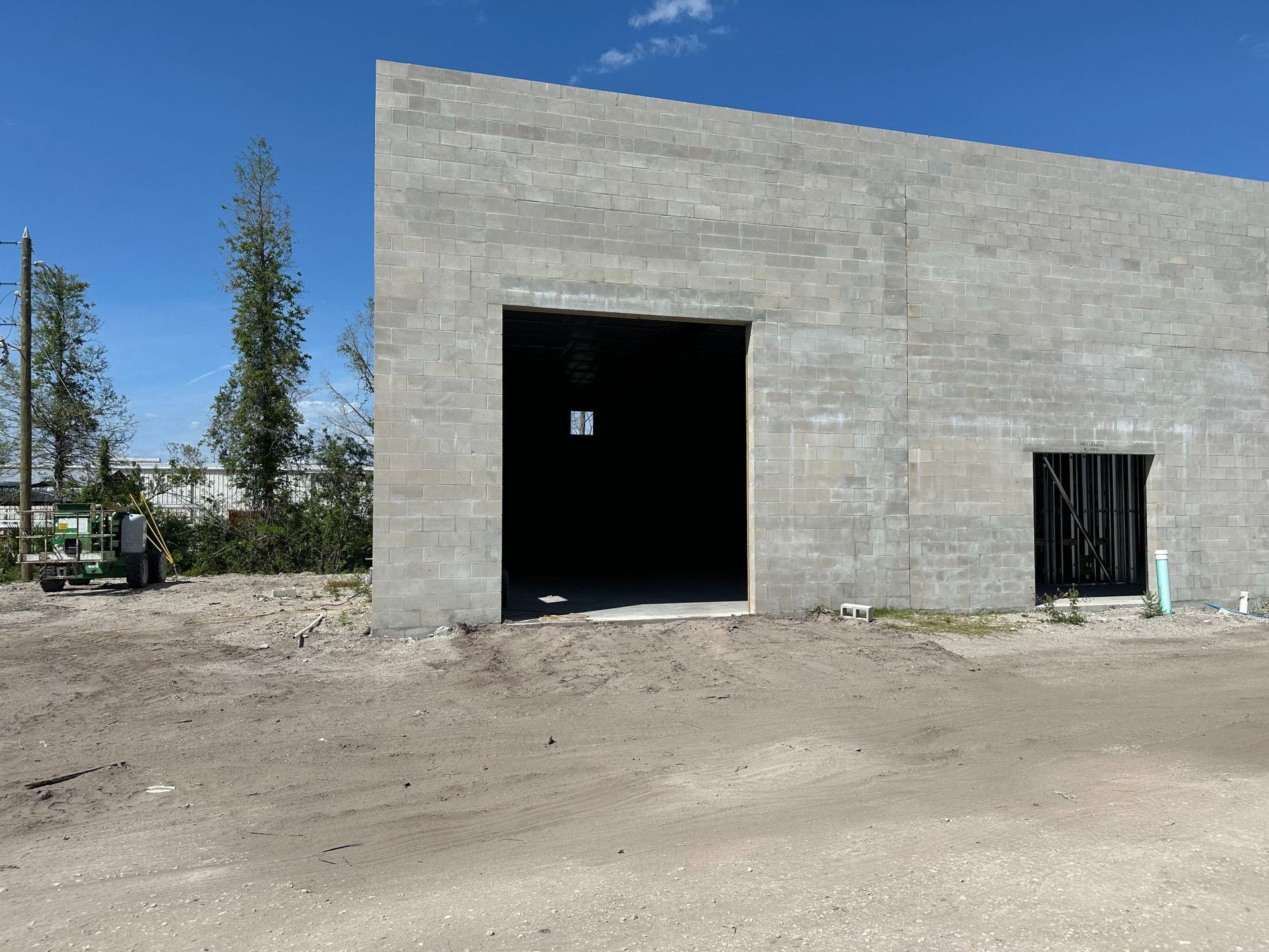 Concrete block building under construction with large open doorway, bright blue sky.