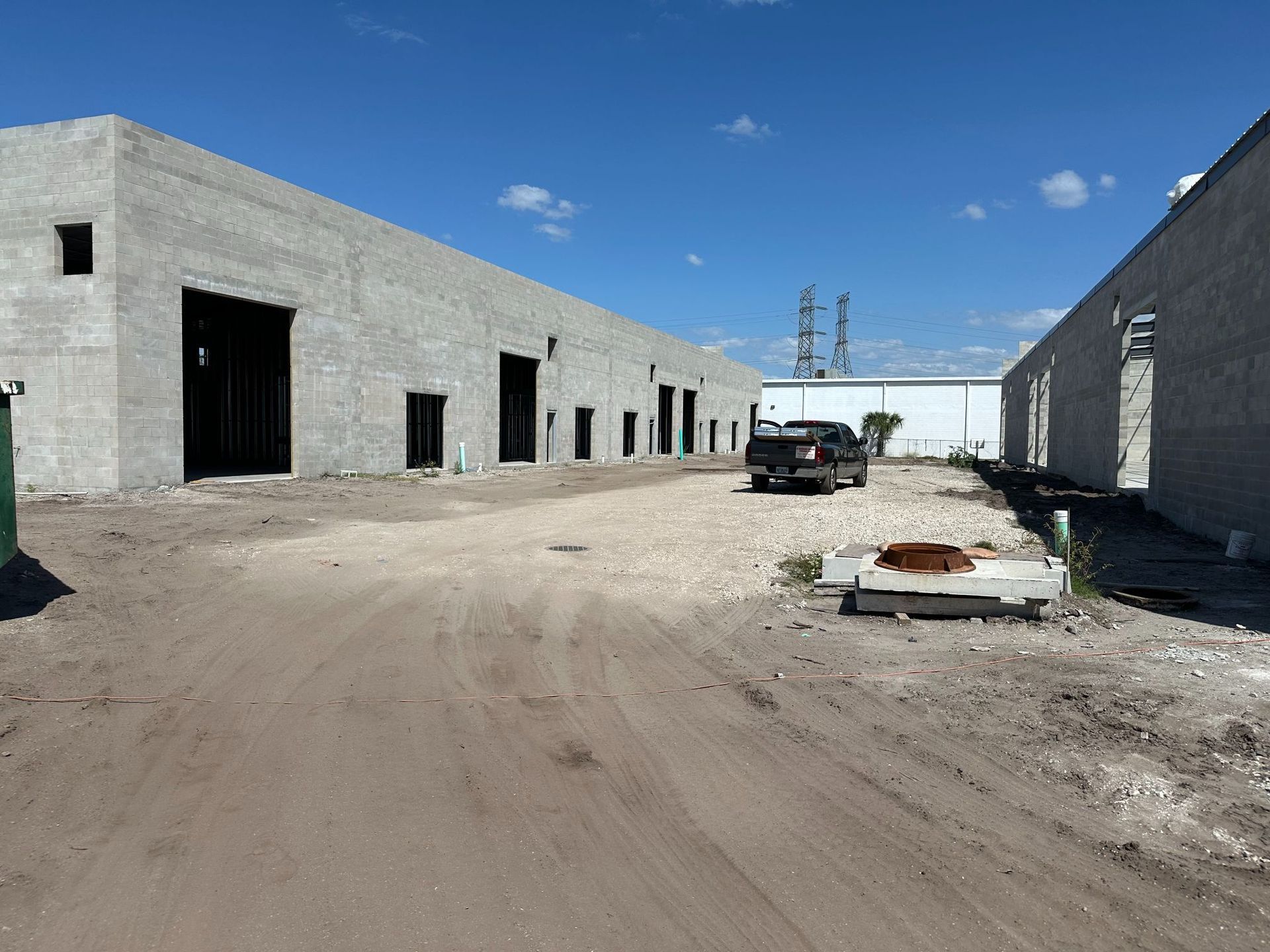 Concrete commercial buildings under construction, dirt road, pickup truck, blue sky.