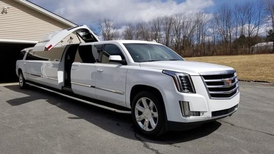 A white cadillac escalade limousine is parked in front of a garage.