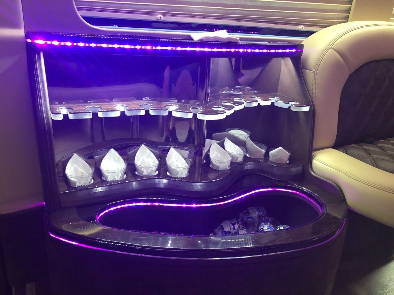 The inside of a limousine with a wine rack and a purple light.