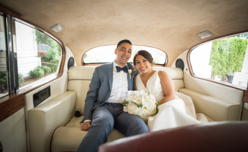 A bride and groom are sitting in the back seat of a car.