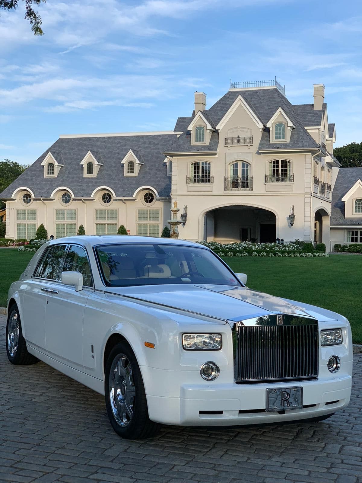 A white limousine is parked in front of a large house.
