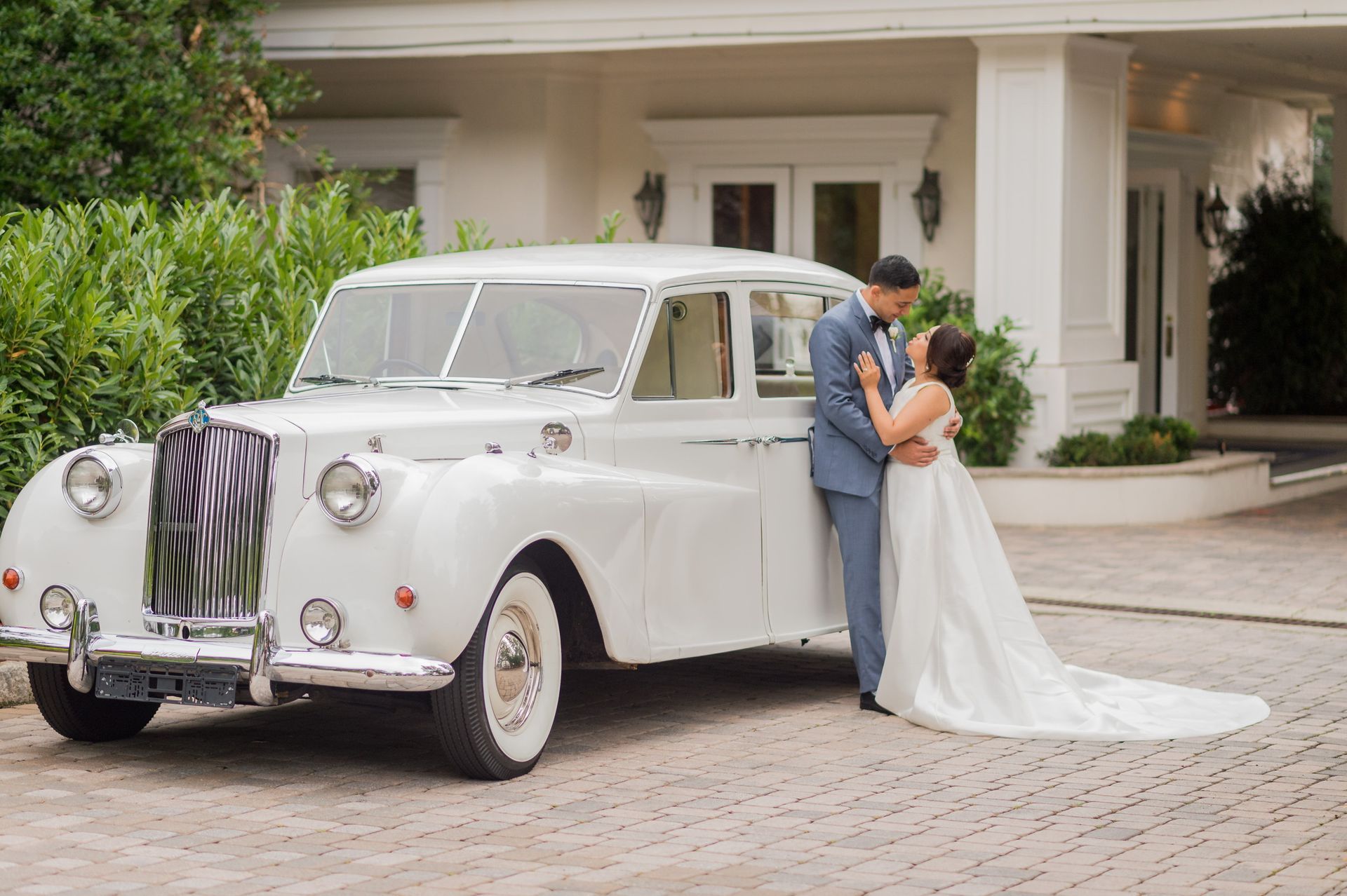 A bride and groom are posing for a picture in front of a white car.