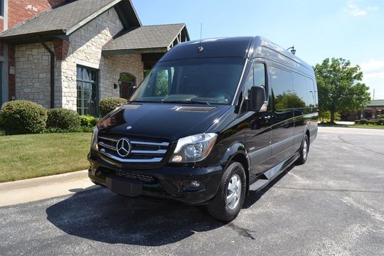 A black mercedes sprinter van is parked in front of a brick house.