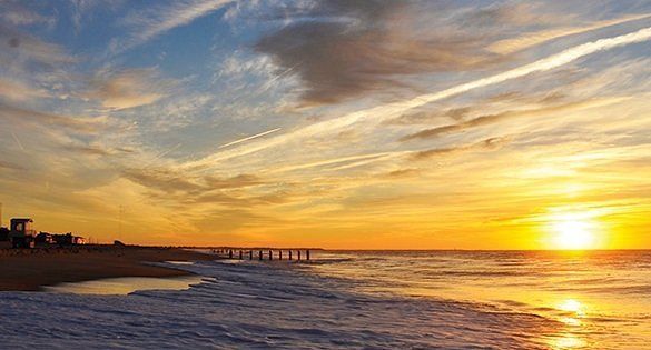 A sunset over a beach with a pier in the background.