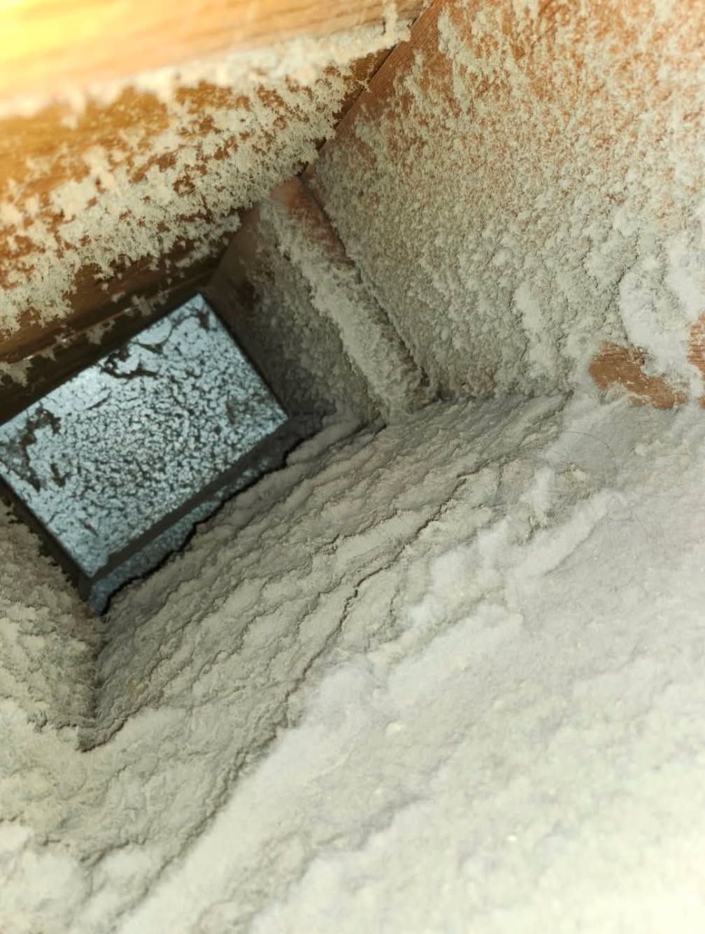 Inside of a dusty air vent. Thick white dust coats the inside of the rectangular duct and vent cover.
