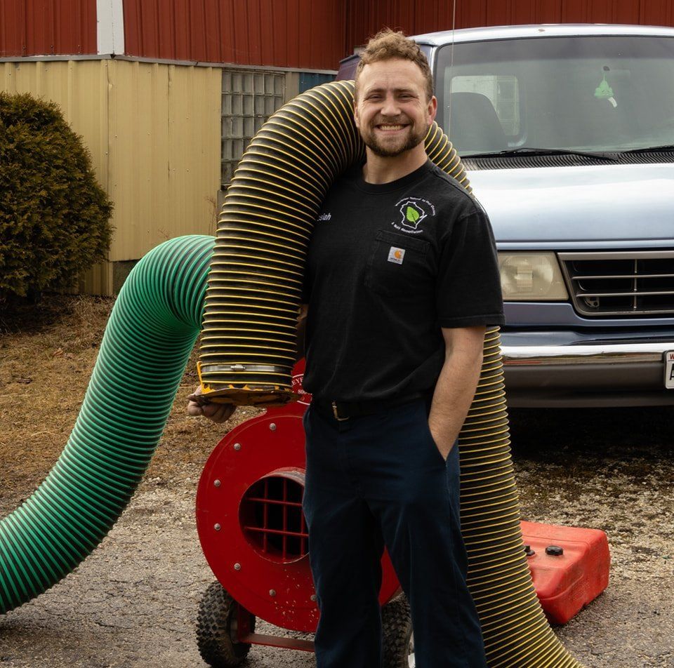 A man in a black shirt is standing next to a large green hose used for air duct cleaning