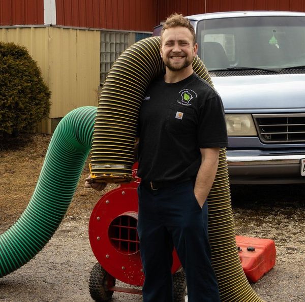 A man in a black shirt is standing next to a large green hose used for air duct cleaning