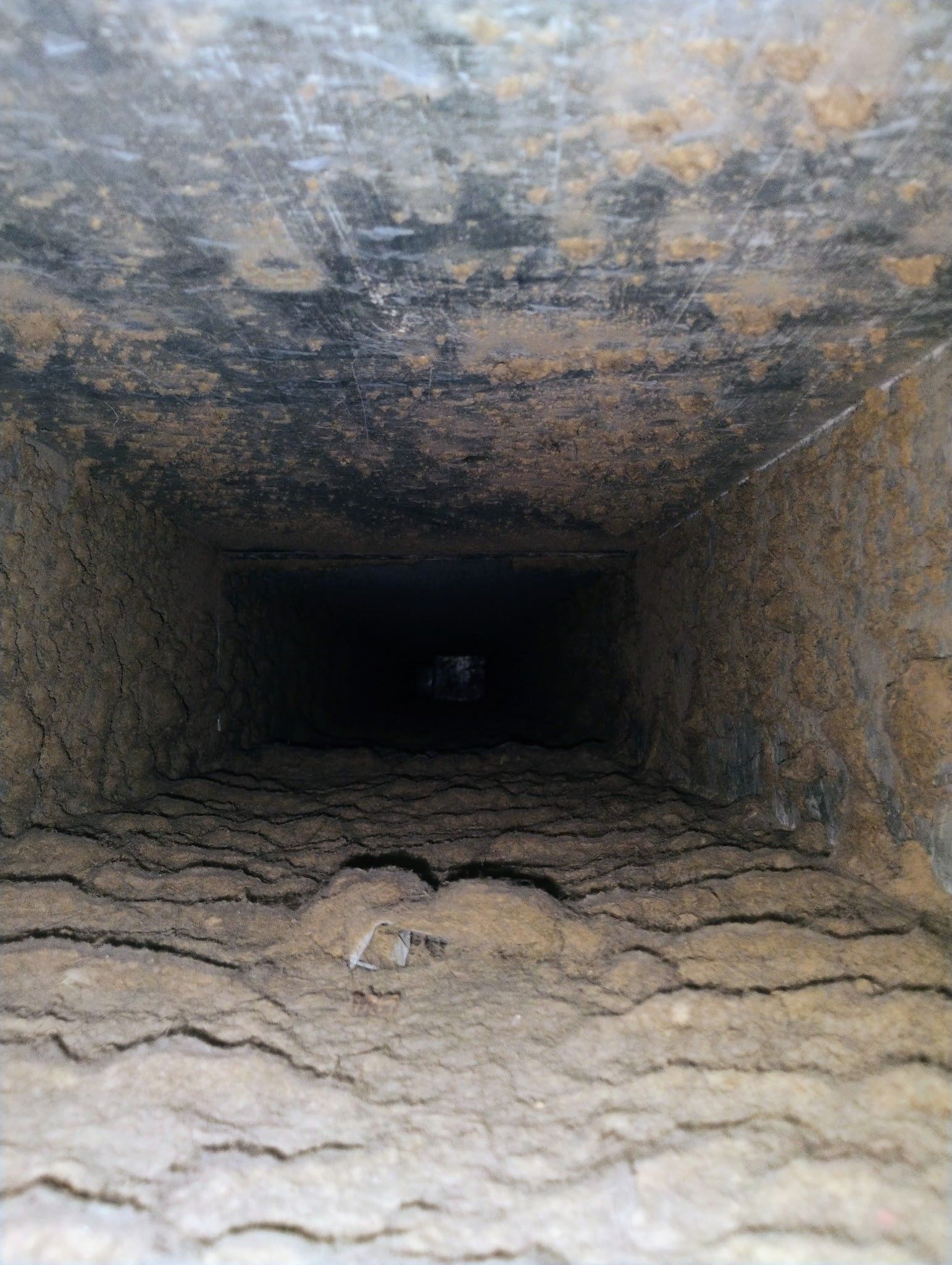 Inside view of a rectangular, dark air duct covered in dust and debris.