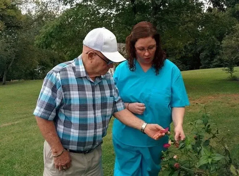 An elderly man and a woman are looking at a flower in a garden.