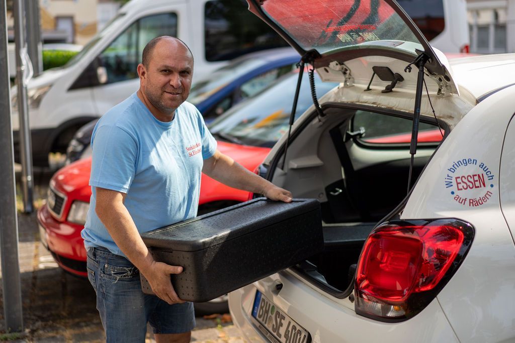 Ein Mann lädt eine Kiste auf den Rücksitz eines Autos.