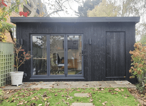 A small black building with a lot of windows is in the backyard of a house.