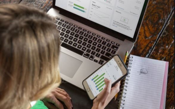 Blonde woman on laptop and smartphone with QuickBooks Online on the screen