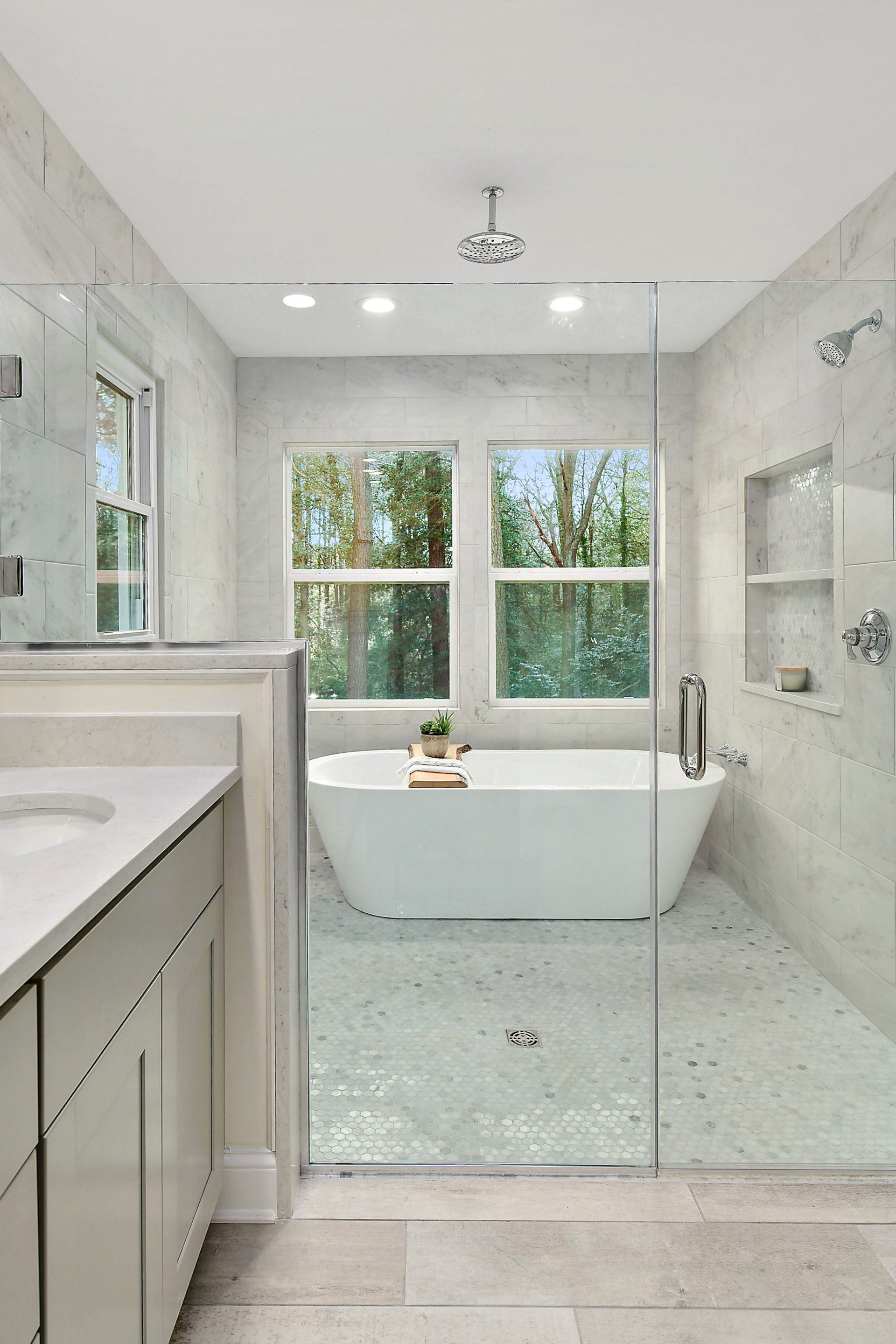 Spacious modern bathroom with a tub near windows, a glass shower, and white cabinetry.