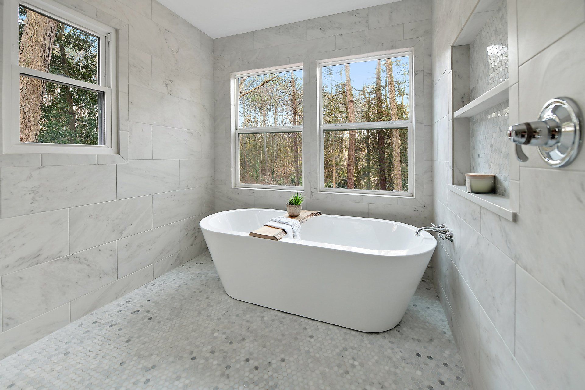 Modern white bathroom with a freestanding tub, two windows, and stone tile.