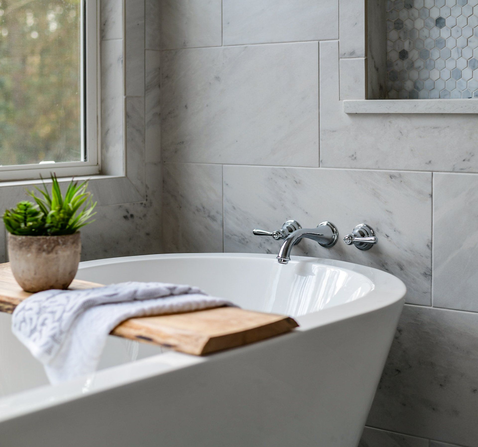Bathroom with white tub, marble walls, and window with a plant.