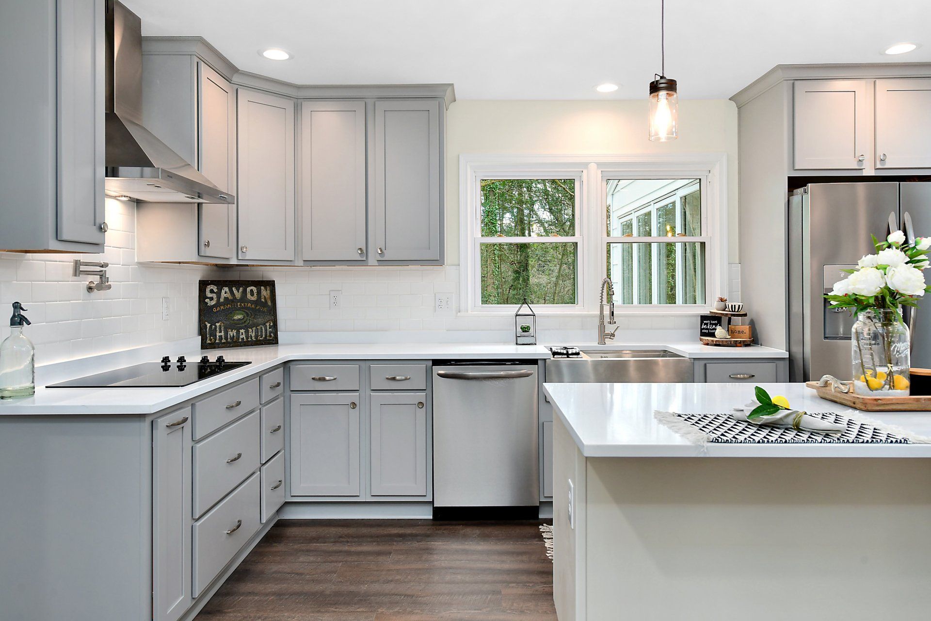 Gray kitchen with white countertops, stainless steel appliances, and a view through a window.