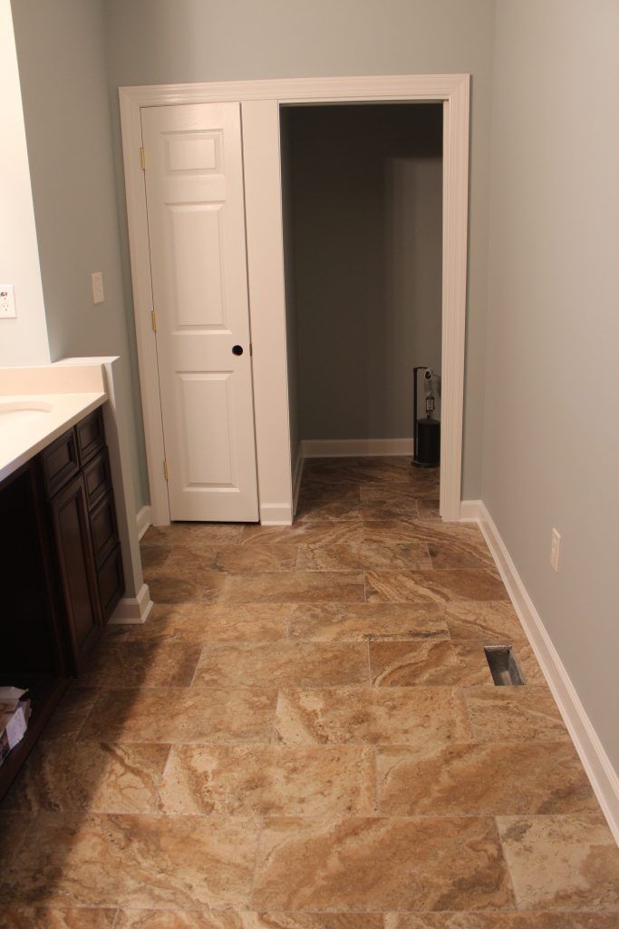 Bathroom with tan tile floor, light blue walls, white trim, and a partially open closet door.