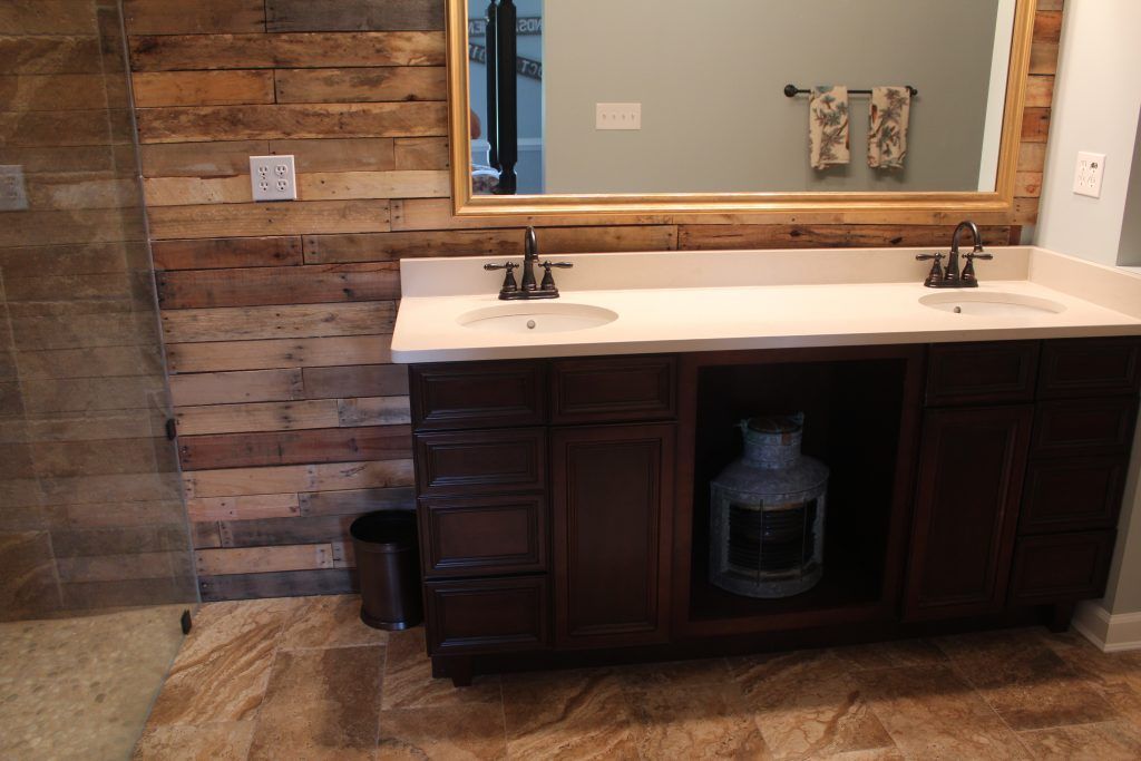 Rustic bathroom with wood-paneled wall, double sink vanity, large mirror, and decorative jar.