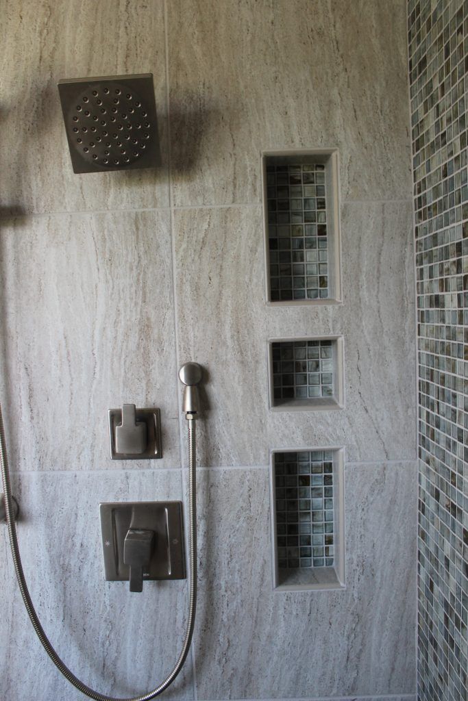 Shower with gray tile, built-in shelves with mosaic tile, and dark metal fixtures.