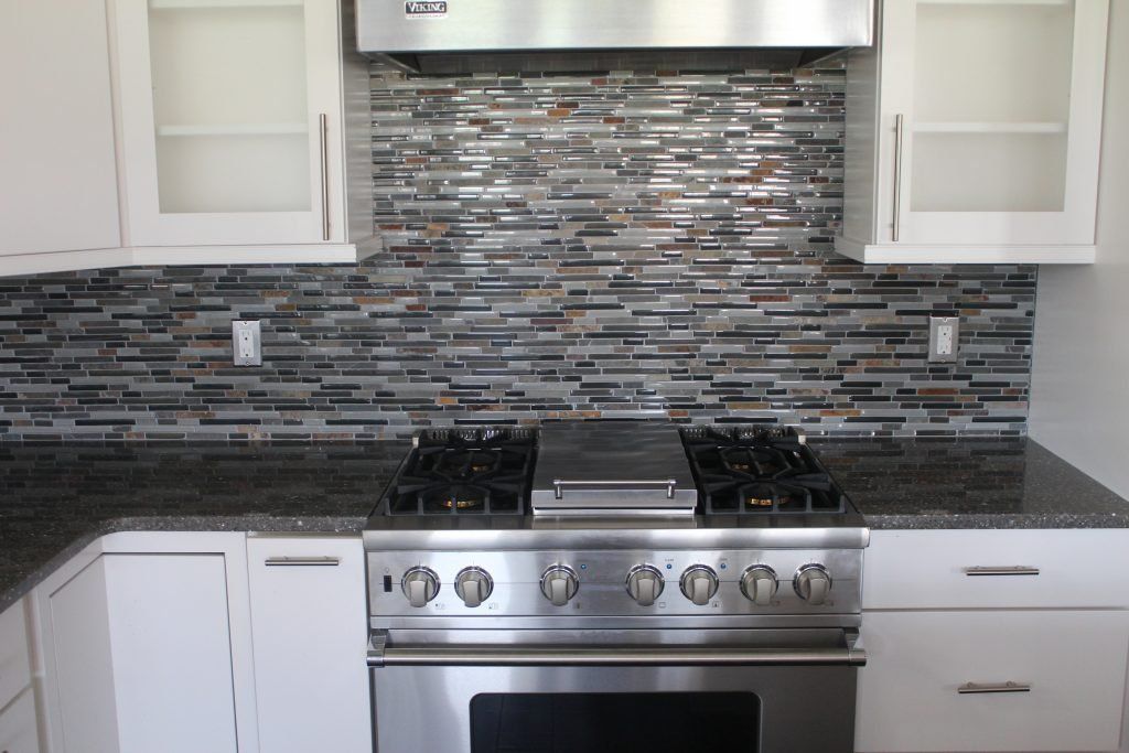 Kitchen with stainless steel stove, dark countertop, and mosaic backsplash. White cabinets above.