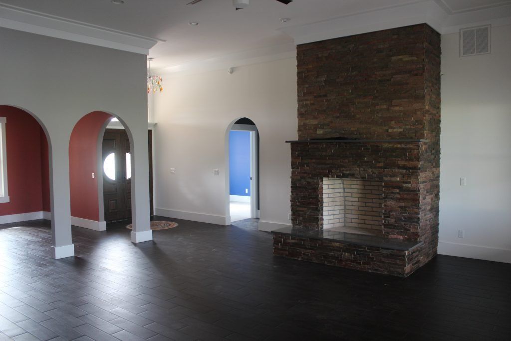 Spacious living room with dark wood floors, brick fireplace, arched doorways with red and blue walls.