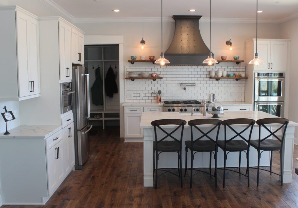 Modern white kitchen with stainless steel appliances, a large island, and wooden floors.