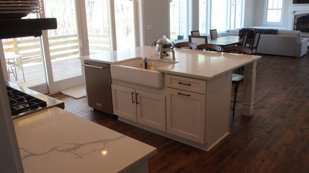 Kitchen island with a white sink, cabinets, and stainless steel dishwasher. Dark wood floors.