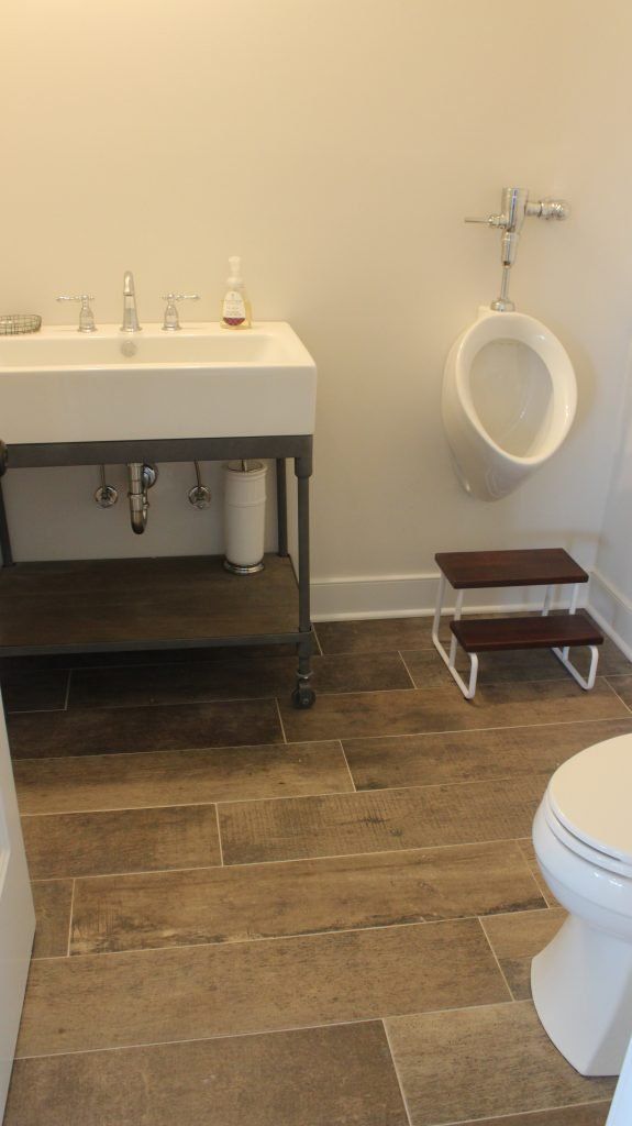 Bathroom with a sink, urinal with a step stool, and a toilet. Wooden floor.