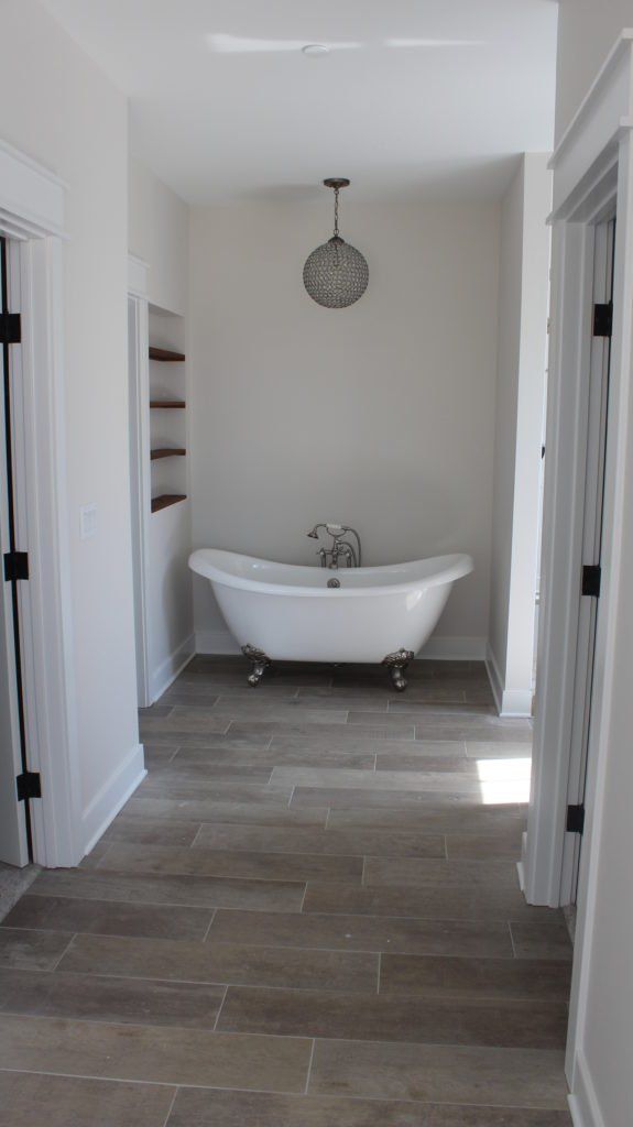 Bathroom with clawfoot tub, light wood floors, white walls, and a decorative clock.