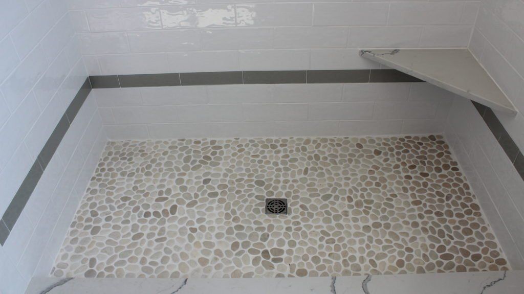Shower with pebble floor and gray tiled walls, with a gray tiled border.