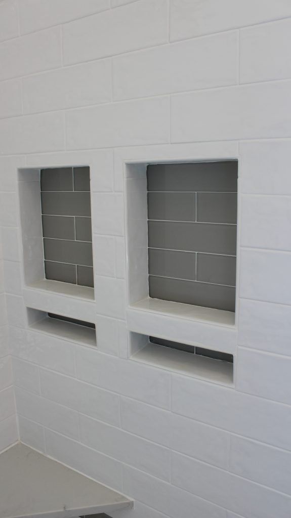 Two gray-tiled recessed niches in a white-tiled wall. Each has a horizontal slot.
