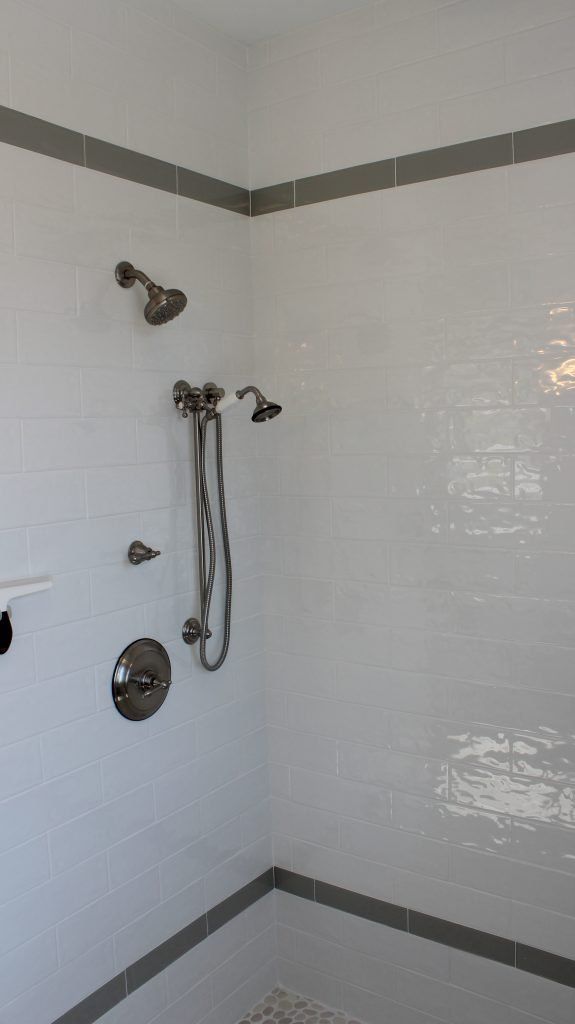 White-tiled shower with gray trim, multiple showerheads and fixtures in a corner setting.