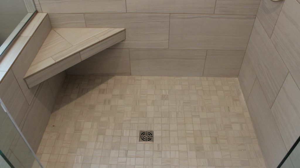 Shower with tiled walls and floor, built-in triangular bench, and drain in the center.