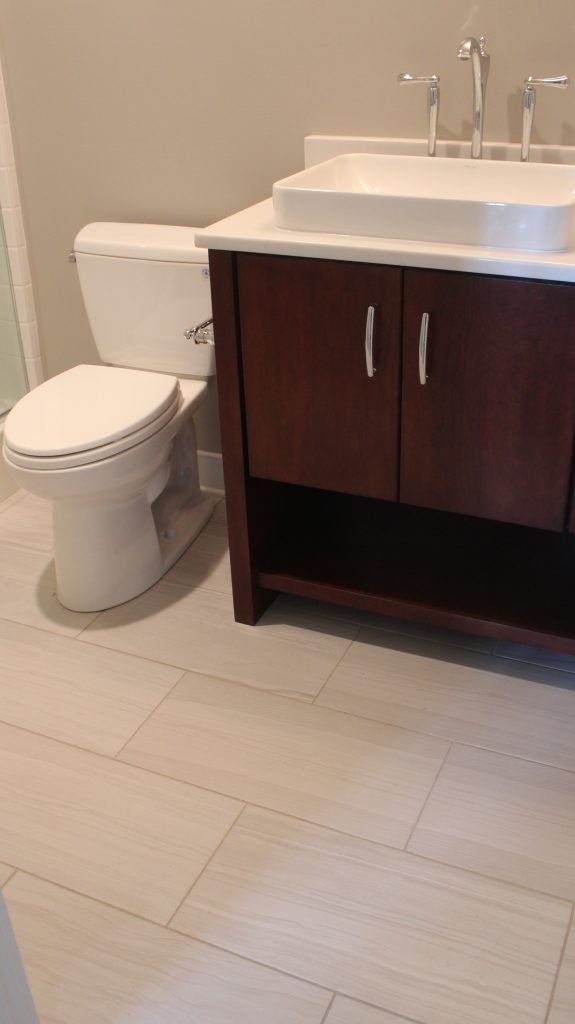 Bathroom with toilet and dark wood vanity with white sink. Light tile floor and light gray walls.