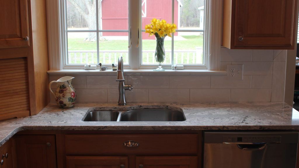 Kitchen sink with a window view of a red barn and yellow flowers in a vase.