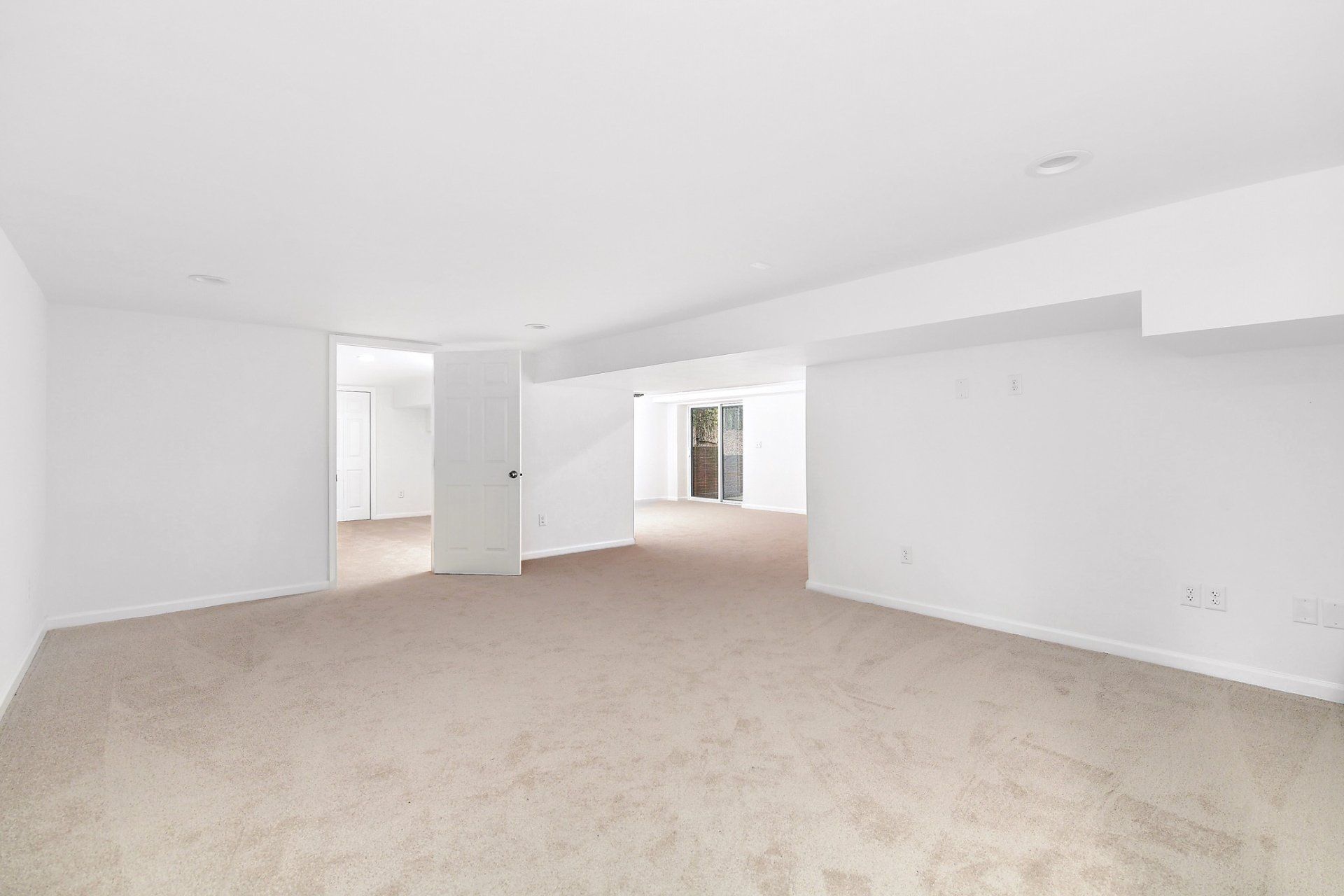 Empty room with beige carpet, white walls, and doorways to other rooms.