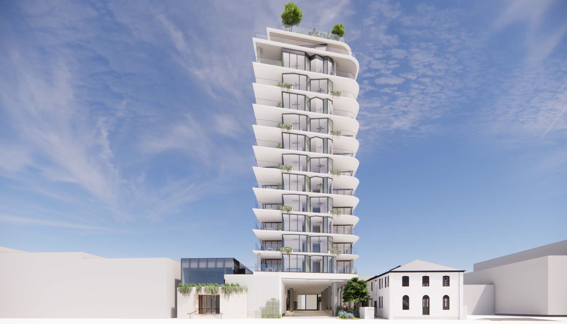 Modern white apartment building with balconies, trees, and small buildings at base against blue sky.