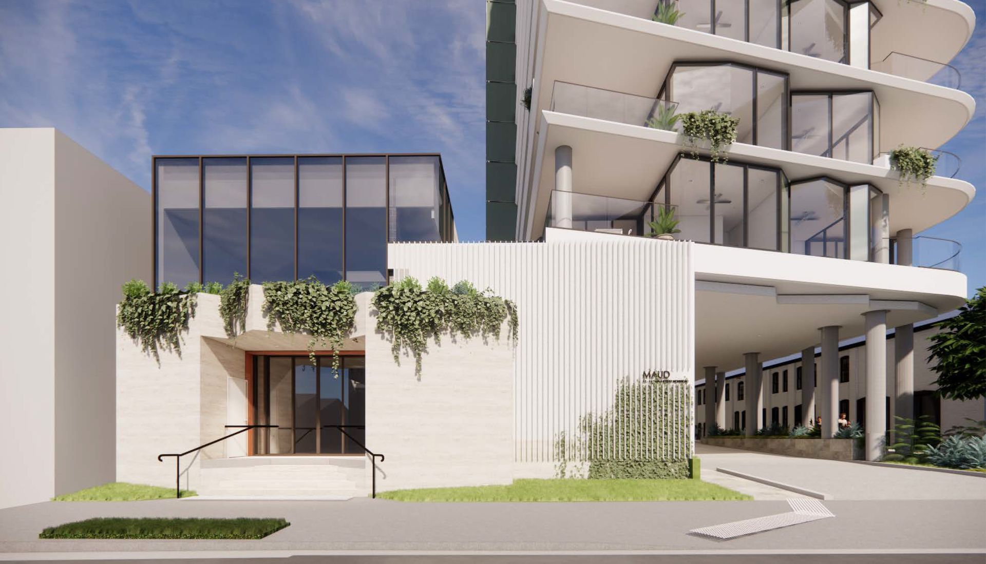Modern building exterior with white walls, glass windows, and greenery. A covered entrance leads to a taller structure.