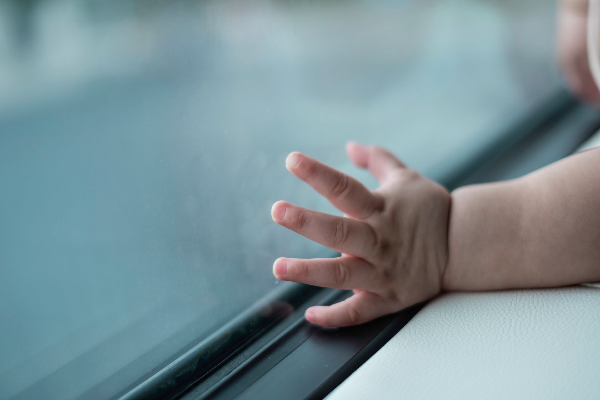 Baby's hand touching a window. Fingers spread, resting on the glass and a white ledge.