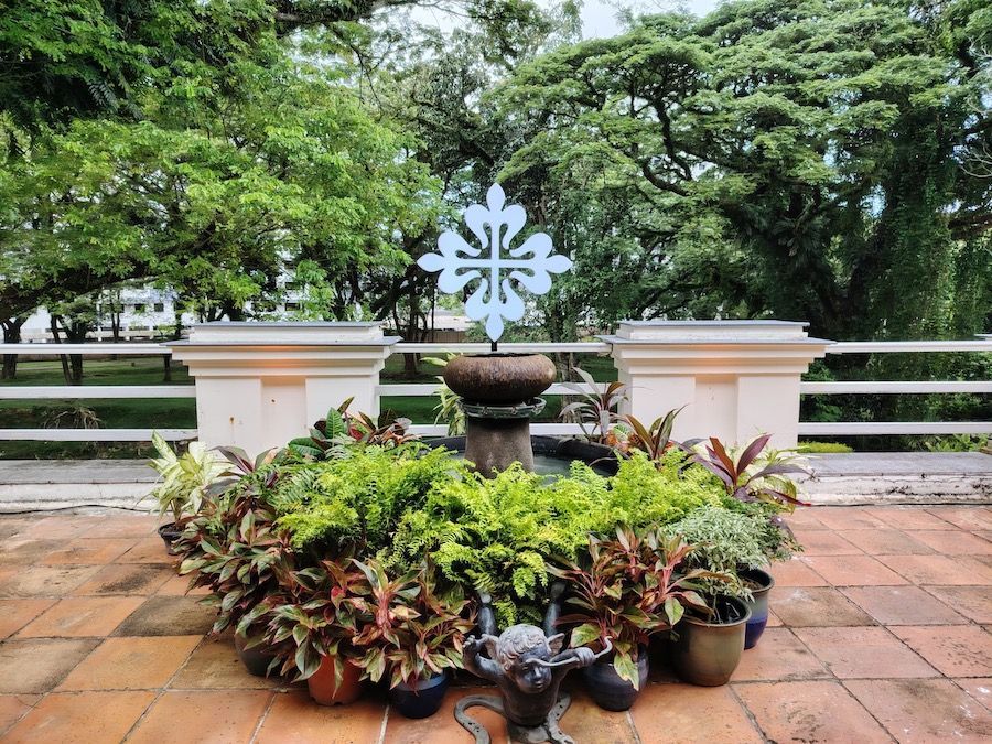 A fountain with a cross on top of it is surrounded by potted plants.