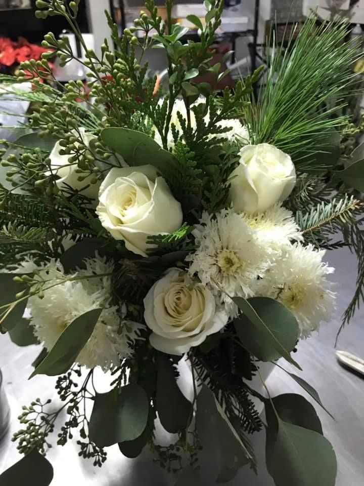 White roses and chrysanthemums with evergreen foliage arranged in a vase.